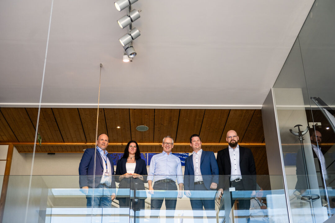 Christopher Ferkl, IT-Leiter bei TEST-FUCHS, Anna Weixlbraun, Support Projektmanagement bei EPS, Volker Fuchs, Geschaeftsfuehrer von TEST-FUCHS, Peter Reisinger, Geschaeftsfuehrer von EPS, und Bernhard Weber, Abteilungsleiter IT-Infrastruktur bei TEST-FUCHS, stehen im oberen Stock auf dem Durchgang und blicken hinunter.