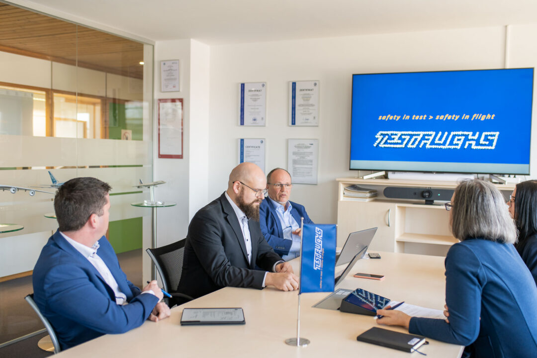 Peter Reisinger, Geschaeftsfuehrer von EPS, Bernhard Weber, Abteilungsleiter IT-Infrastruktur bei TEST-FUCHS, Christopher Ferkl, IT-Leiter von TEST-FUCHS, Anna Weixlbraun, Support Projektmanagement bei EPS und Irene Mondon-Stutterecker sitzen gemeinsam bei Tisch und fuehren ein Interview.